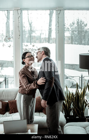 Hohe grauhaarige stattlicher Mann in ein blaues Hemd und eine dunkelhaarige Frau Gefühl wunderbare Stockfoto