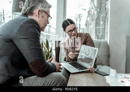 Dunkelhaarige elegante Frau in einem braunen Satin Bluse mit Diagramm auf einem Laptop Stockfoto