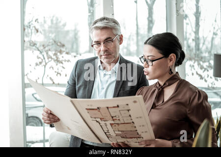 Dunkelhaarige elegante Frau in einem braunen Satin Bluse und ihr Geschäftspartner konzentriert Stockfoto