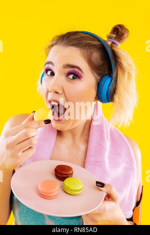 Frau sich nicht der Kontrolle nach dem Fitnessstudio beim Essen Macaron Stockfoto