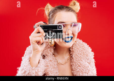 Frau mit blauen Lippen und rosa Schlafbrillen mit Kamera Stockfoto