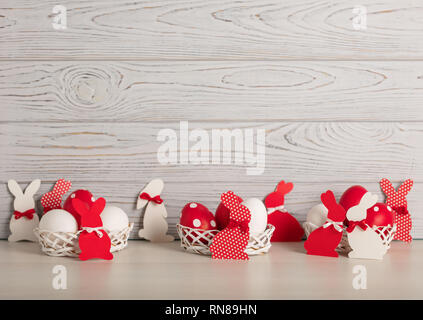 Frohe Ostern! Bemalte Ostereier und Osterdekoration - Osterhasen mit Bändern - Rot, Weiß und Rot mit weißen Tupfen auf einem grauen Holz zurück Stockfoto
