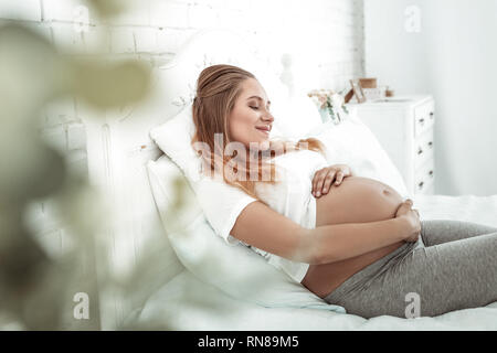 Ruhige langhaarigen schwangere Frau ihren glatten Bauch berühren Stockfoto