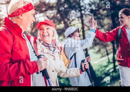 Figurbetonte Frau. Bärtige pensionierter Mann umarmte seine nette attraktive Dame beim Nordic Walking zusammen Stockfoto