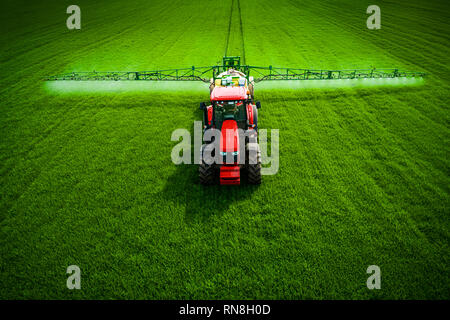 Фarming Traktor Pflügen und Spritzen auf grünes Weizenfeld, Antenne drone Ansicht Stockfoto