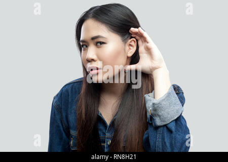 Portrait von aufmerksamen schöne Brünette asiatische junge Frau in casual blaue Jacke mit Make-up stehen die Hand in der Nähe des Ohrs und versuchen zu Spion oder Liste Stockfoto