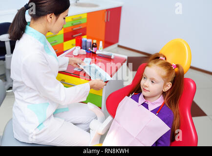 Kinder Zahnarzt untersucht die Zähne und Mund des Kindes - ein süßes rothaariges Mädchen in einem behandlungsstuhl Sitzen Stockfoto