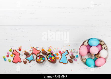 Ostern Grußkarte mit bunten Lebkuchen Kekse, Schokolade, Eier, Süßigkeiten und Ostern Eier in der Schale. Draufsicht auf hölzernen Tisch mit Platz für Ihre Stockfoto