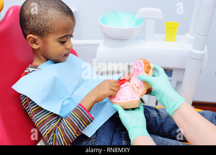 Ein pädiatrischer Zahnarzt lehrt einen afrikanischen amerikanischen Kind, das in einem Behandlungsstuhl sitzt, um seine Zähne zu putzen. Stockfoto