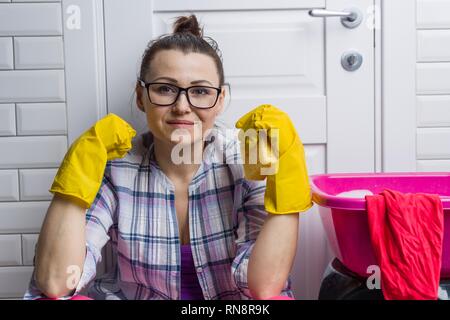 Hausfrau Frau ist die Reinigung im Bad. Schaut in die Kamera, geduckt in der Nähe der Tür, neben dem Waschbecken, Lumpen. Stockfoto