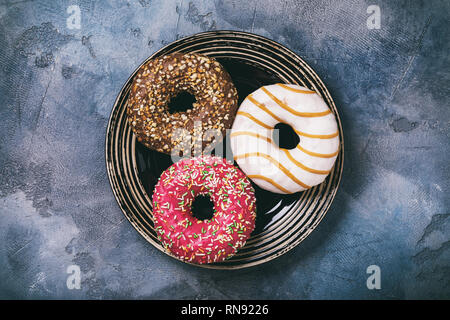 Drei Donuts mit Erdbeer, Schokolade und Karamell in eine Platte auf Tabelle, Ansicht von oben Stockfoto