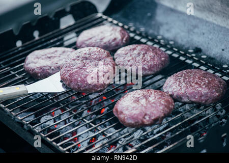 Selektiver Fokus der Spachtel und rohe frische Burger schnitzel Grillen auf bbq-Raster Stockfoto