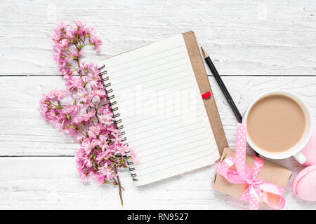 Frühling rosa blühenden Blumen mit leeren Papier notepad, Macarons, Kaffeetasse und Geschenkbox auf weissem Holztisch. Flach. Ansicht von oben mit Platz für Te Stockfoto