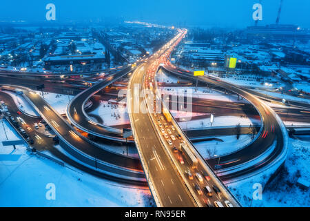 Luftaufnahme von der Straße in der modernen Stadt bei Nacht im Nebel. Blick von oben auf den Verkehr in der Landstraße. Winter Stadtbild mit erhöhten Straße, Autos, Gebäude, Illumina Stockfoto