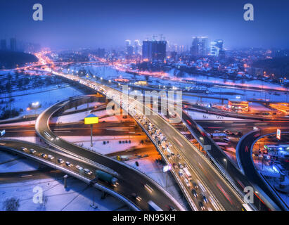 Luftaufnahme von der Straße in der modernen Stadt bei Nacht im Nebel. Blick von oben auf den Verkehr in der Landstraße. Winter Stadtbild mit erhöhten Straße, Autos, Gebäude, Illumina Stockfoto