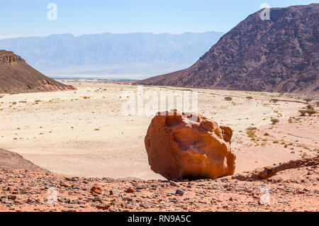Riesige Stein liegt am Rande des Hügels mit felsigen Wüstenlandschaft in Timna Nationalpark in Aravah Tal in Israel. Stockfoto
