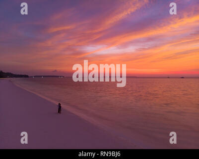 Antenne: Paar beobachten Sonnenuntergang Himmel sitzen auf Sand Strand romantische Himmel bei Sonnenuntergang, Rückansicht, golden cloudscape, echte Menschen umarmen sich. Indonesien, Kei isl Stockfoto