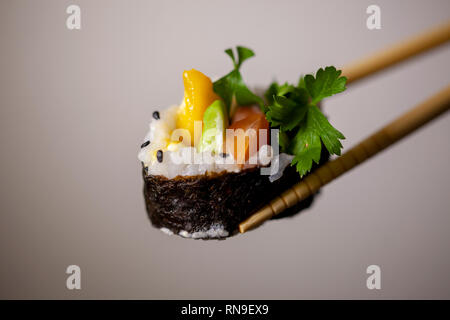 Hausgemachte brasilianische Sushi mit Mango, Lachs und Avocado mit Stäbchen gegen eine saubere grauen und weißen Hintergrund gehalten Stockfoto
