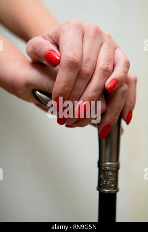 Weibliche Hände mit einem roten Maniküre Holding einen Stock. Close-up. Stockfoto