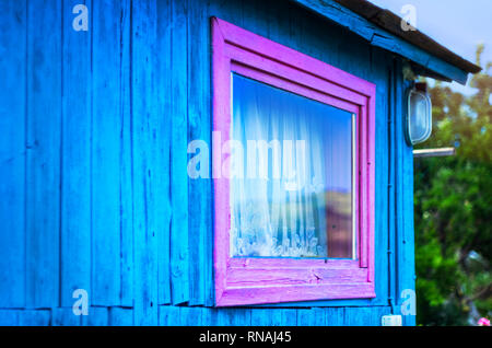 Minimalistisches Design Konzept: Vivid Lila Fensterrahmen, ein Licht auf blauen Wand der hölzernen Planken. Berge Reflexion in Glas, weißem Vorhang. Dachkehlen. Stockfoto