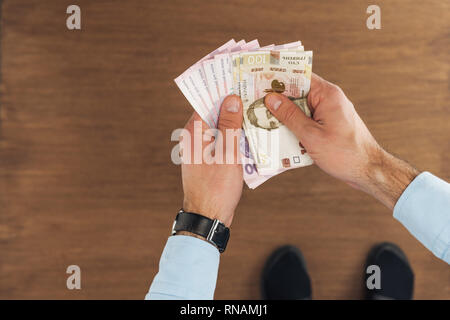 Blick von oben auf die Mann hält Griwna Banknoten auf hölzernen Hintergrund Stockfoto