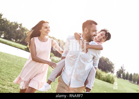 Kleben. Familie von drei Fuß auf Wiese Vater mit Sohn auf seinem wieder ein Lächeln glücklich Stockfoto