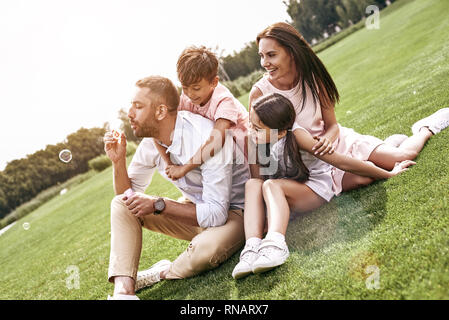 Kleben. Familie von vier Sitzen auf einer Wiese Seifenblasen lächelt glücklich Stockfoto