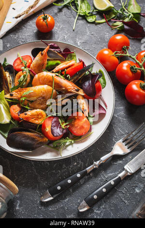 Frische Meeresfrüchte, Salat, Muscheln, Garnelen, frischem Gemüse und Kräutern auf schwarzen Stein Hintergrund Stockfoto