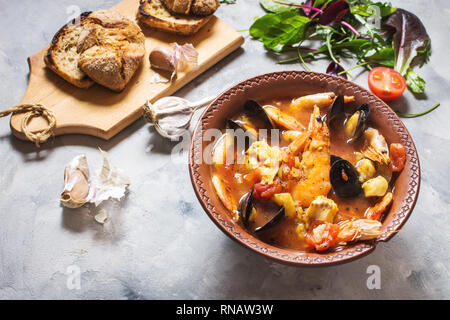 Französische Fischsuppe bouillabaisse mit Meeresfrüchten, Lachsfilet, Garnelen, Muscheln auf konkreten Hintergrund. Köstliches Abendessen Stockfoto