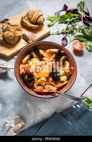 Französische Fischsuppe bouillabaisse mit Meeresfrüchten, Lachsfilet, Garnelen, Muscheln auf konkreten Hintergrund. Köstliches Abendessen Stockfoto