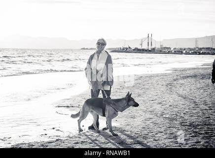 Schönen Ruhestand ältere Frau und pet-deutscher schäferhund Hund wandern entlang der Küste Meer Ozean am Strand in Begleitung Nutzen der Tiere aktiv halten Stockfoto