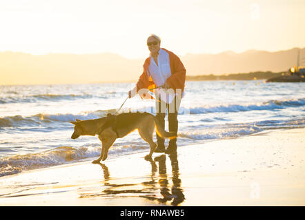 Schönen Ruhestand ältere Frau und pet-deutscher schäferhund Hund wandern entlang der Küste Meer Ozean am Strand in Begleitung Nutzen der Tiere aktiv halten Stockfoto