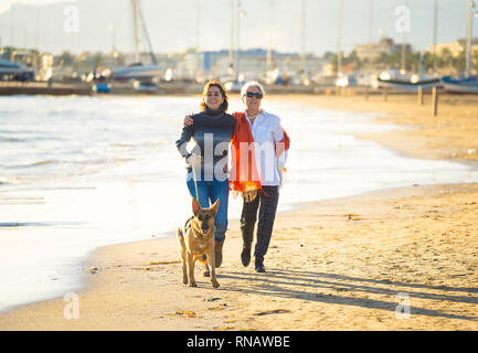 Gerne ältere Mutter ihre erwachsene Tochter und Deutscher Schäferhund hund Ausgabe Zeit zusammen zu Fuß am Strand bei Sonnenuntergang Licht in der glücklichen Familie Momente Pet-Anim Stockfoto