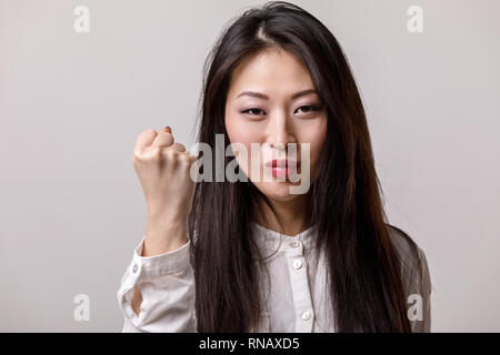 Portrait der asiatischen Frau in Weiß Shirt, Faust auf grauen Hintergrund. Emotionen Stockfoto