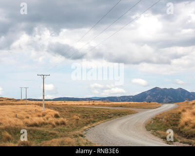 Strommasten Linien auf Biegung eine unversiegelte Schotterstraße, tussock Land, Ngamatea Station, Inland Mokai Patea, Central North Island, Neuseeland Stockfoto