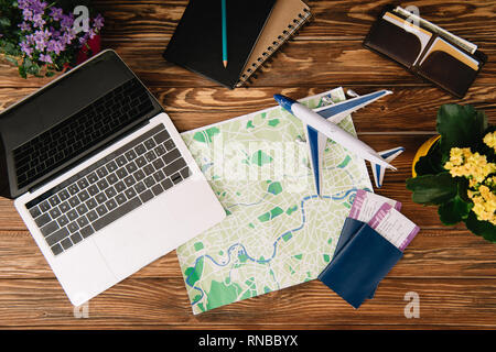 Blick von oben auf die Laptop, Karte, Pässe mit Tickets und Flugzeug Modell auf Holz- Oberfläche Stockfoto