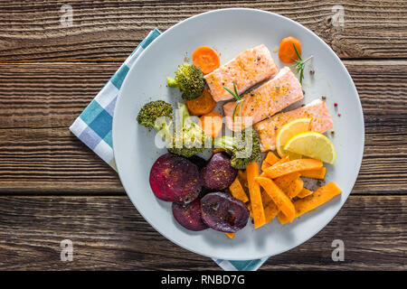 Schmackhaftes Gericht mit gekochtem Gemüse, gegrillter Lachs und Pommes frites auf Teller, Ansicht von oben Stockfoto