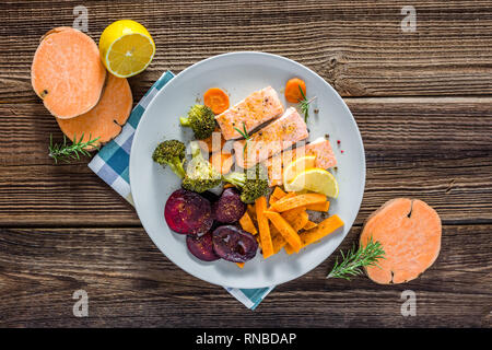 Gebackener Lachs mit Gemüse. Gekochtes Fischfilet mit Pommes frites auf Teller, Ansicht von oben Stockfoto