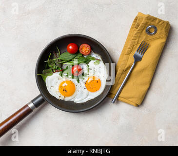 Pfanne mit zwei Spiegeleier, Kräuter, Tomaten, die Schaltgabel und die Serviette auf weißem Hintergrund Stockfoto