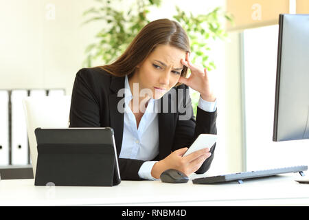 Besorgt Büroangestellter arbeiten mit mehreren Geräten auf einem Schreibtisch Stockfoto