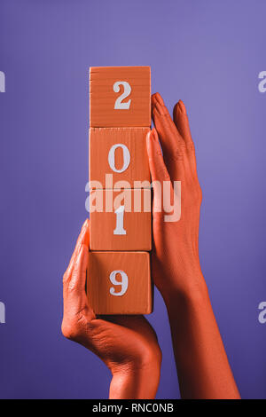 Teilweise mit Blick auf die Frau mit coral Holzwürfel mit 2019 Nummern auf blauem Hintergrund, Farbe 2019 Konzept Stockfoto