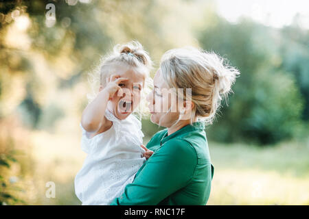 Junge Mutter tröstet weinende kleine Tochter im Sommer in der Natur. Stockfoto