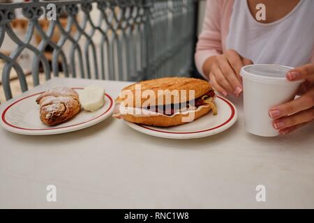 Licht und herzhaften Frühling Frühstück. Croissant mit Schinken, Käse, frische Tomaten auf einem weißen Tisch. Mädchen und Kaffee Stockfoto