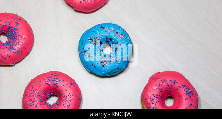 Blau und Rosa glasierten Krapfen mit Streuseln auf hellen Hintergrund, Ansicht von oben. Stockfoto