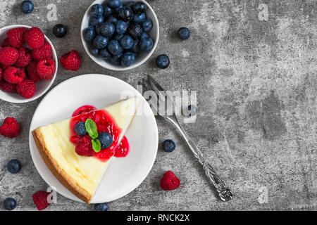 Scheibe der New Yorker Käsekuchen mit frischen Himbeeren, Heidelbeeren, Marmelade und Minze mit Gabel auf konkreten Hintergrund. top anzeigen. Leckeres Frühstück Stockfoto