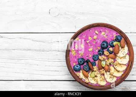 Gesund vegan Frühstück. acai Smoothie Schüssel mit Blaubeere, Obst, Müsli, Mandeln, Kürbis und Chia Samen auf weissem Holztisch. detox food Konzept Stockfoto