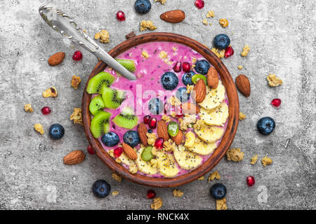 Acai smoothie Schüssel gekrönt mit Blaubeere, Früchte, Chia und Kürbiskerne, Mandeln und Müsli mit Löffel. gesund vegan Frühstück. top View Stockfoto