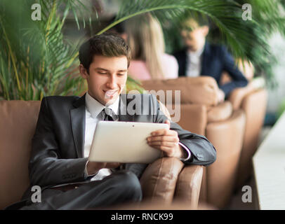 Unternehmer - Anfänger mit einem digitalen Tablet sitzen auf der Couch in der Lobby eines modernen Büro Stockfoto