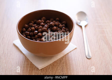 Schokolade mais Kugeln in Milch zum Frühstück. Gießen Milch mit Spritzern von Tropfen in eine Schüssel mit knusprigen Frühstückscerealien reich an Weizen, Hafer und Kleie, Stockfoto