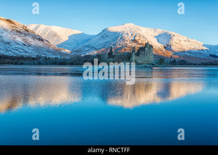 Am frühen Morgen bei Kilchurn Castle und Loch Awe, Argyll und Bute, Schottland, Großbritannien an einem kalten Wintertag mit Schnee und die Sonne nur die Beleuchtung der Berge Stockfoto